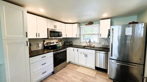 A modern kitchen with white cabinets, stainless steel appliances, and a herringbone-patterned backsplash. - New! Sandy Point-Private beach/Dog Friendly (Eastham)