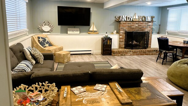 A living room with a sectional sofa, a fireplace, a flat-screen TV, and a dining area. - New! Sandy Point-Private beach/Dog Friendly (Eastham)