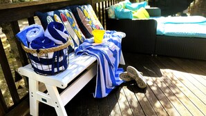A wooden deck with a white bench, a basket of folded towels, and a yellow bucket. - New! Sandy Point-Private beach/Dog Friendly (Eastham)