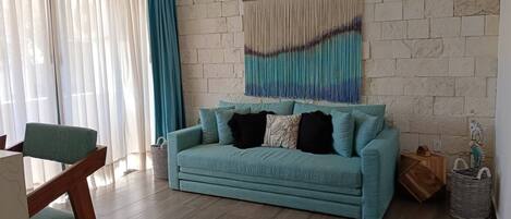 Un salón con sofá color turquesa, suelo de madera, pared de piedra y una gran obra de arte abstracta.