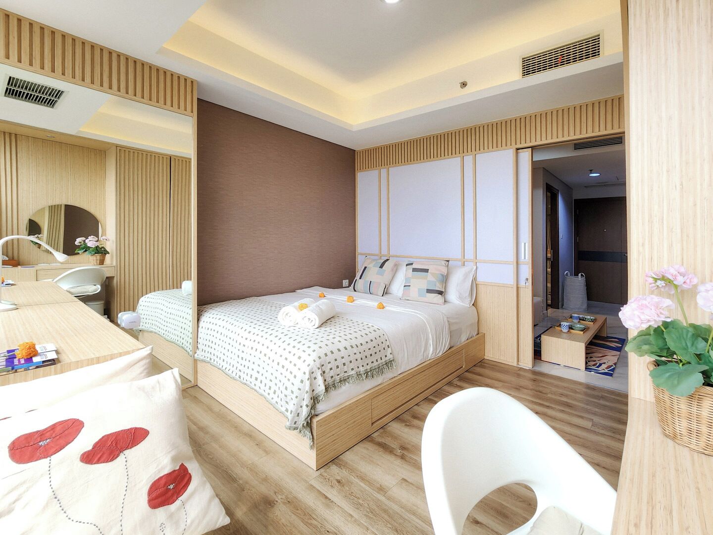 A modern hotel room with a wooden bed, a desk, a chair, and a large mirror.