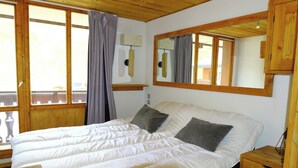 A bedroom with a large bed, wooden headboard, a nightstand, a mirror, and a window with curtains.