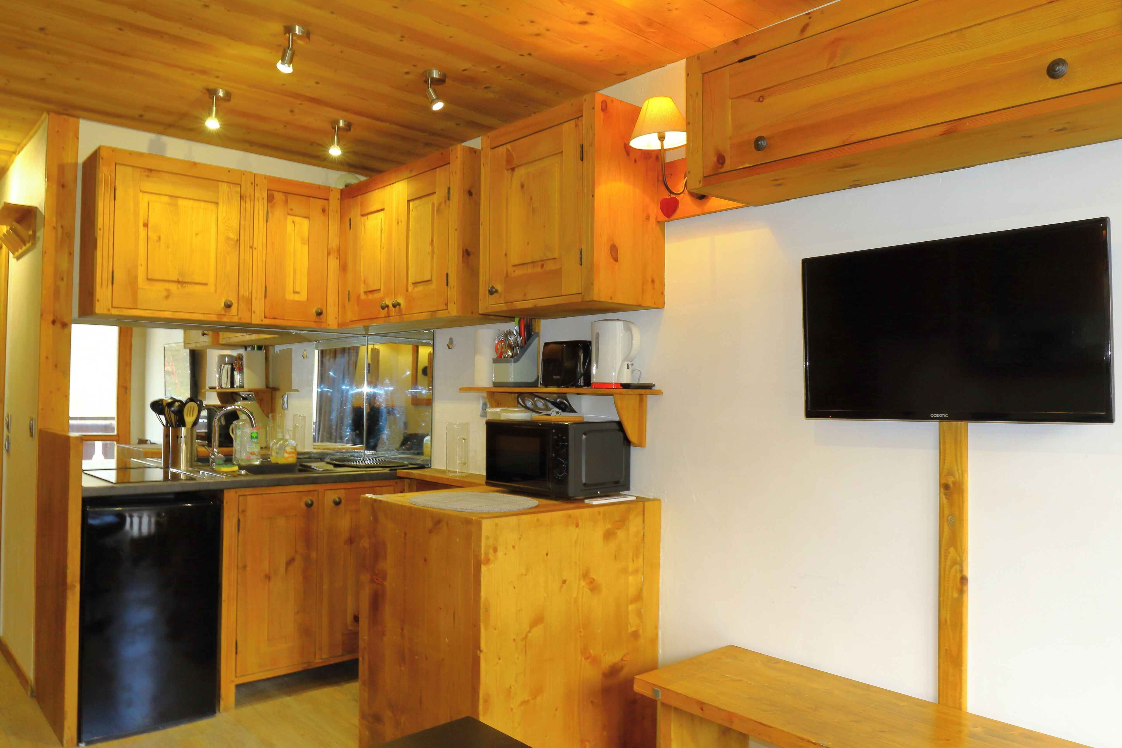 Una cocina con armarios de madera, microondas, fregadero y televisor de pantalla plana negro montado en la pared.