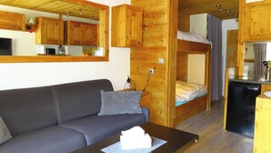 A compact room with a sofa, a bunk bed, a small kitchenette, and wooden walls.
