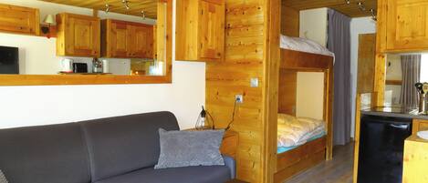 Ein gemütlicher Raum mit einer Sitzecke, einem Etagenbett, einer kleinen Küchenzeile und Holzwänden.