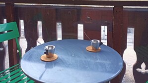 A round table with two metal cups on coasters, green chairs, and a view of a mountainous landscape.
