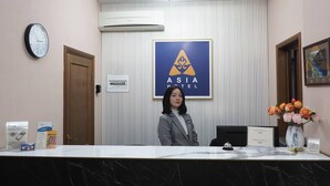 A reception desk with a clock, a framed logo, a vase of flowers, and a sign indicating room rates.