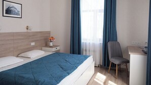 A hotel room with a bed, a desk, a chair, and a window with curtains.