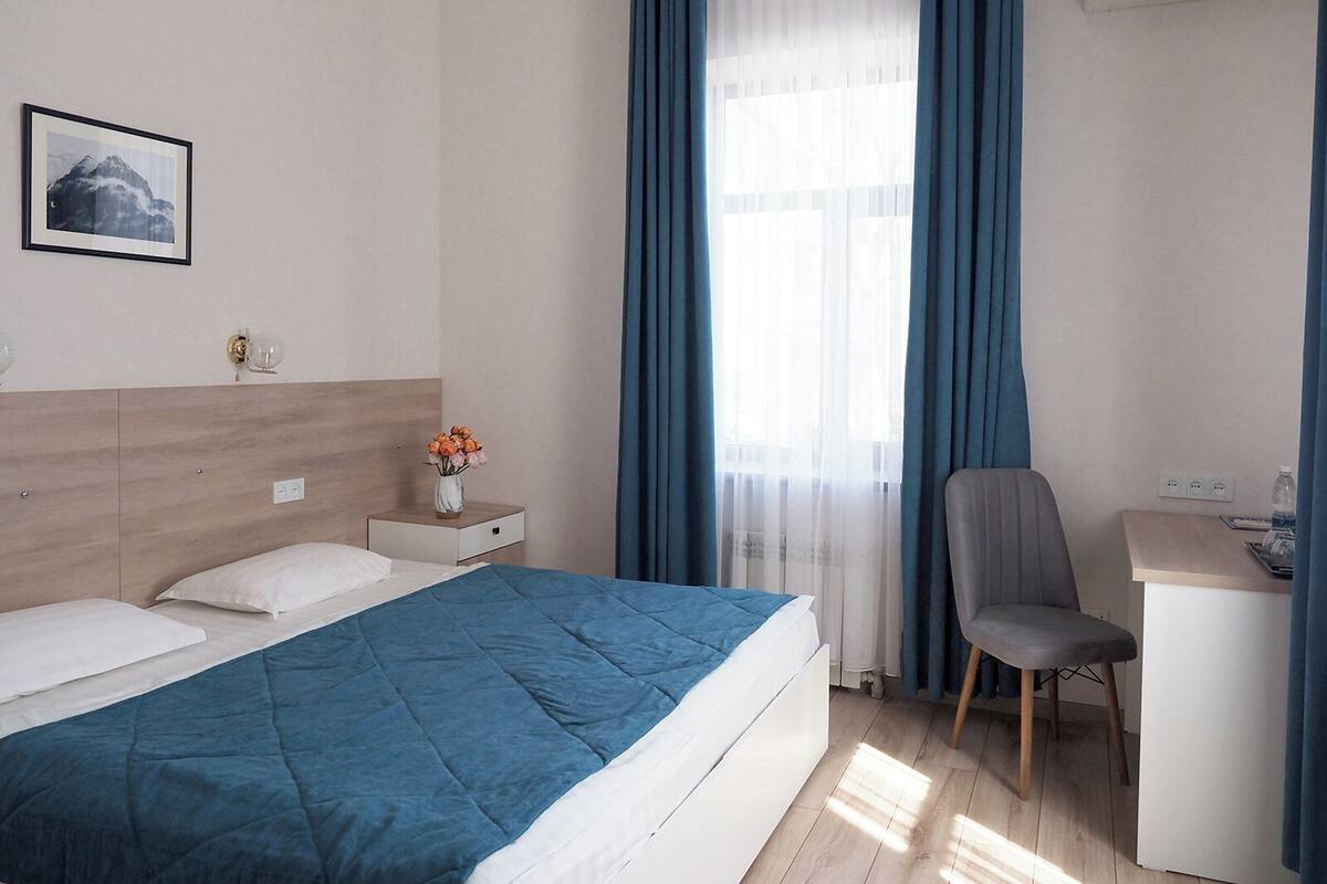 Ein Hotelzimmer mit Bett, Schreibtisch, Stuhl und einem Fenster mit Vorhängen.