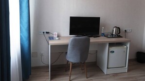 A small, modern room with a desk, a computer, a chair, a mini-fridge, and a kettle.