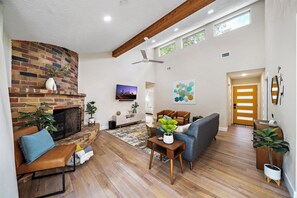 Uma sala de estar com lareira, piso de madeira, um sofá, uma mesa de centro e uma televisão.