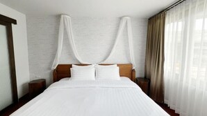 Een groot bed met houten hoofdeinde, witte beddengoed en een hemelbed. Er staan twee nachtkastjes met lampen.