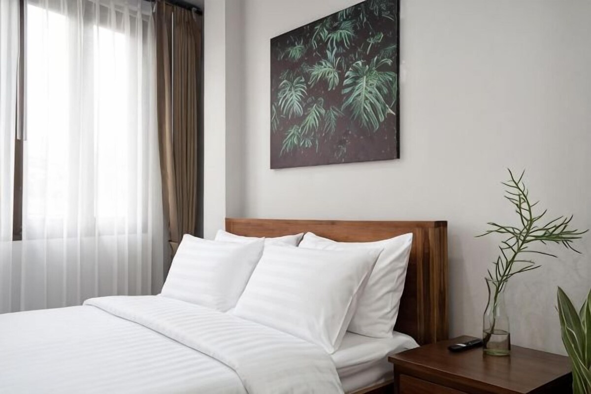 A hotel room with a bed, a nightstand, a remote control, and a wall-mounted plant.