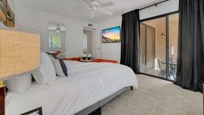 A hotel room with a large bed, a ceiling fan, a view of the outdoors, and a sliding glass door to the balcony.