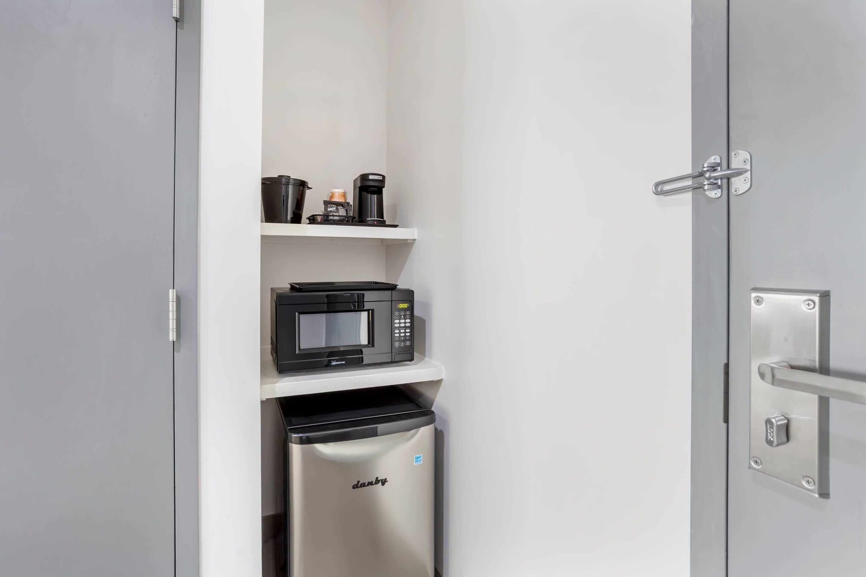 A compact kitchen with a microwave, coffee maker, and a trash bin.