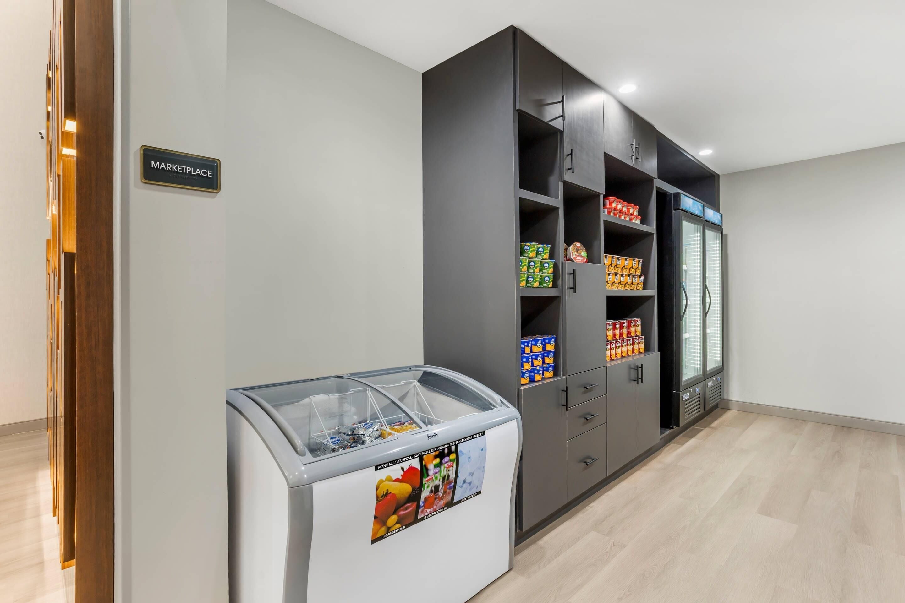 A kitchenette area with a freezer, a refrigerator, and a pantry stocked with beverages and snacks.