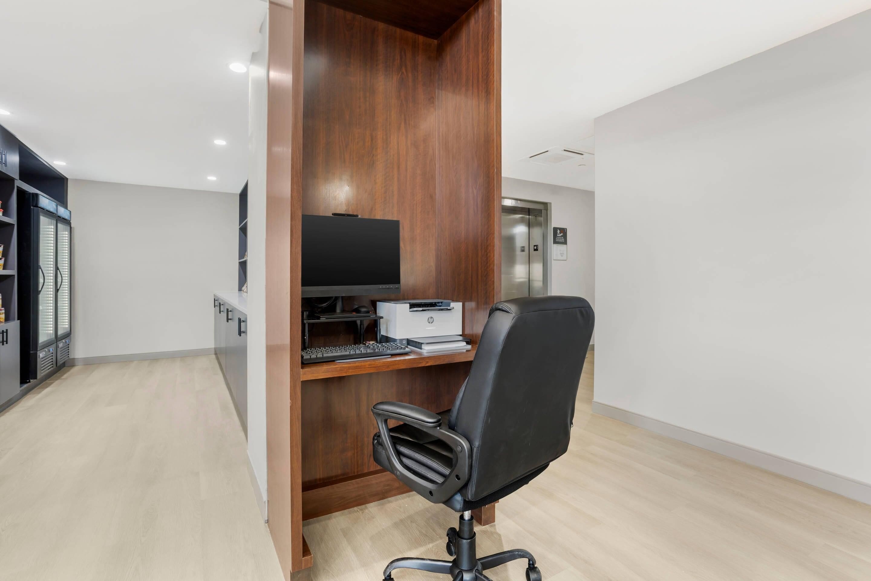 A modern office space with a wooden desk, a black office chair, a flat-screen TV, and a printer.