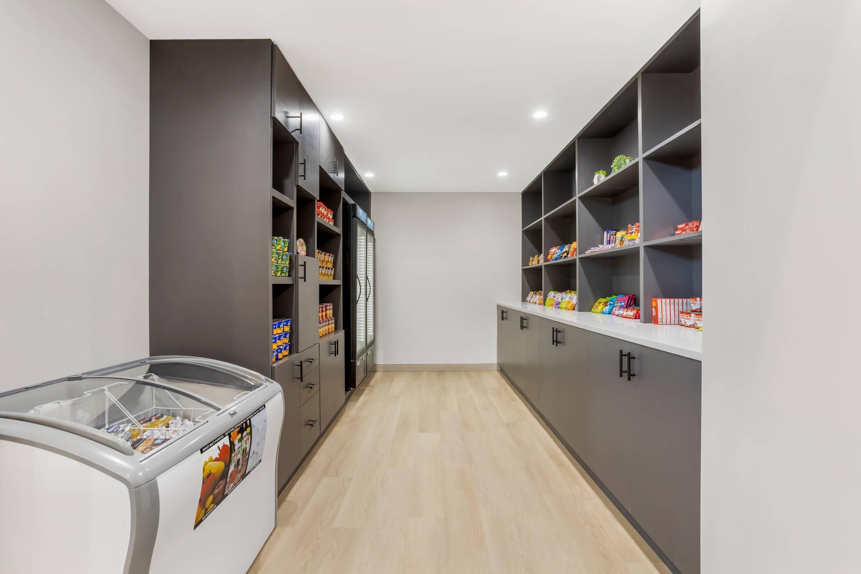 A narrow hallway with a freezer on the left and shelves stocked with snacks on the right.
