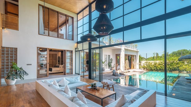 A spacious living area with a large sofa, a wooden coffee table, and a view of a swimming pool through large glass windows. - Villa Lava (Canggu)