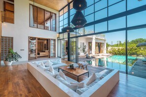 Amplia sala de estar con un sofá grande, una mesa de centro de madera y vistas a una piscina a través de grandes ventanales.