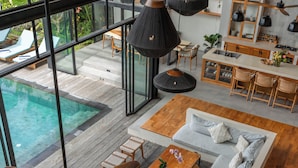A modern interior with a wooden floor, a large sofa, a dining area, and a view of an outdoor pool. - Villa Lava (Canggu)
