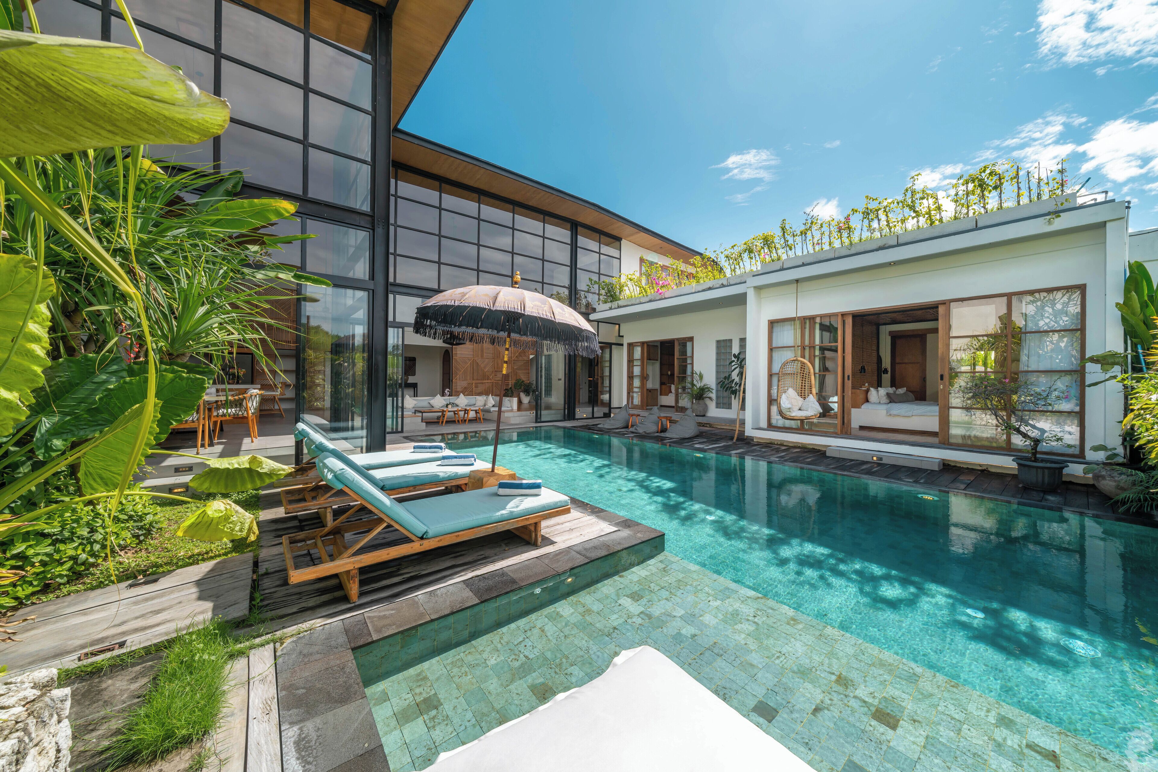 A modern pool area with lounge chairs, a covered seating area, and a large window overlooking the pool.