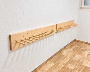 A wooden drying rack mounted on a textured white wall.