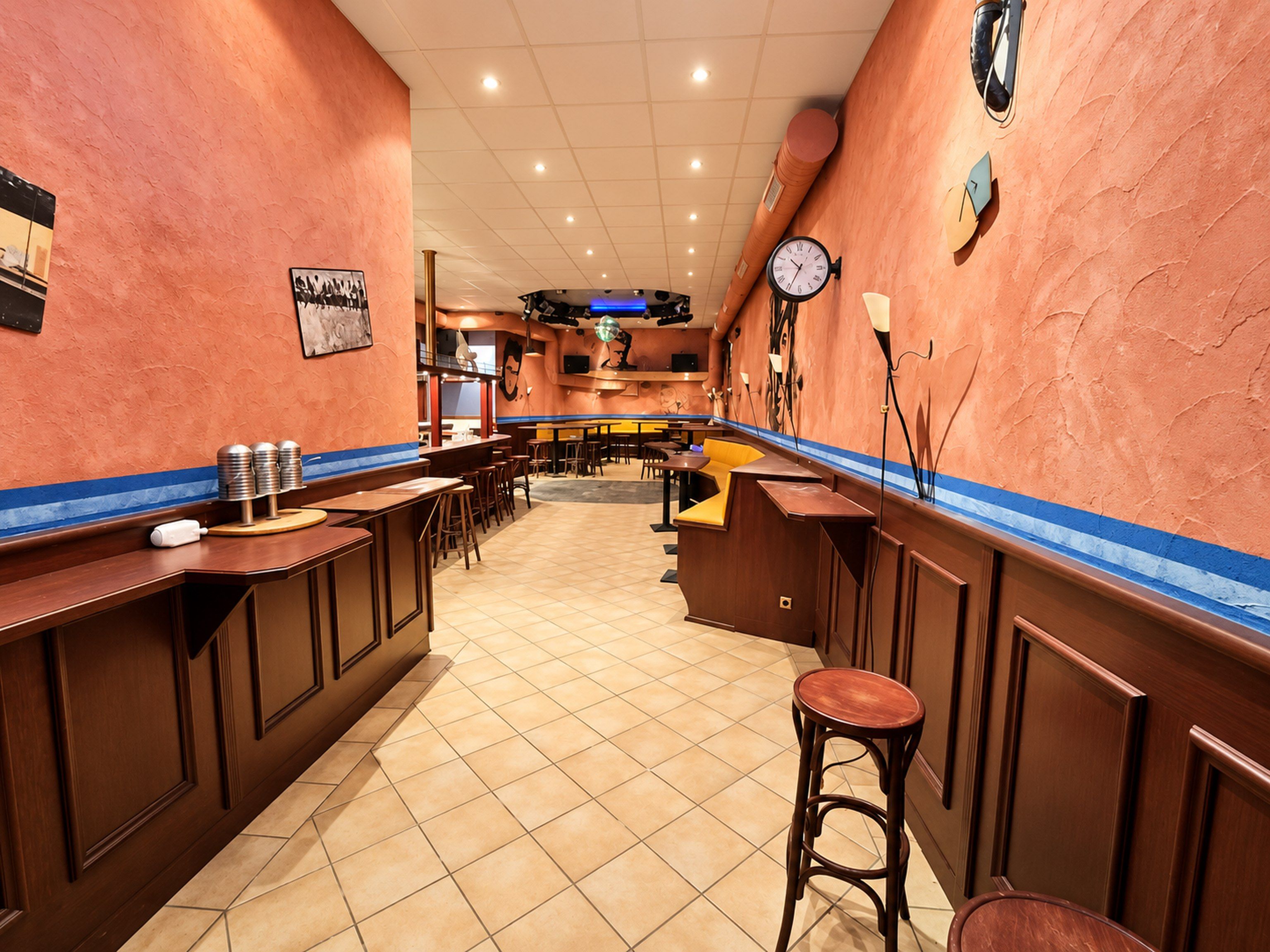 Ein Restaurantinnenraum mit einer langen Theke, Hockern und einer Uhr an der Wand.