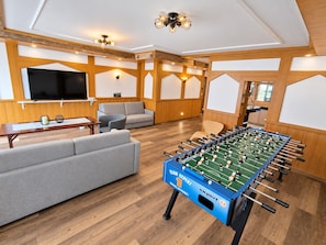 A room with a foosball table, sofas, a TV, and wooden paneling.