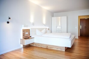 A modern bedroom with a wooden platform bed, a nightstand, a wardrobe, and a mirror. - Comfortable and versatile room -perfect for relaxation, work and exchange (Winterberg)
