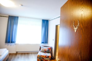 A hotel room with a bed, a small table, and a wooden door with a deer head emblem.