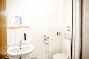 A bathroom with a white sink, toilet, and a glass shower enclosure. - Comfortable and versatile room -perfect for relaxation, work and exchange (Winterberg)
