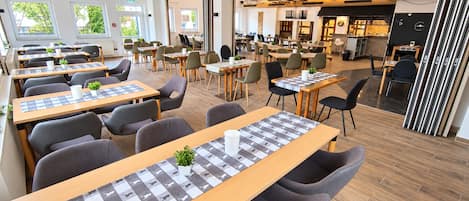 Un comedor moderno con varias mesas y sillas, una zona de cocina y vistas al exterior.