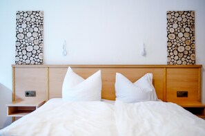A double bed with white bedding, wooden headboard, bedside tables, and wall-mounted light switches. - Comfortable and versatile room -perfect for relaxation, work and exchange (Winterberg)