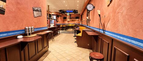 A restaurant interior with a long counter, stools, and a clock on the wall.