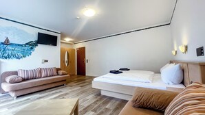 A modern hotel room with a wooden floor, a bed with white linens, a sofa with striped cushions, and a wall-mounted TV.