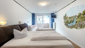 A hotel room with a large bed, a flat-screen TV mounted on the wall, and a balcony with a view of buildings.