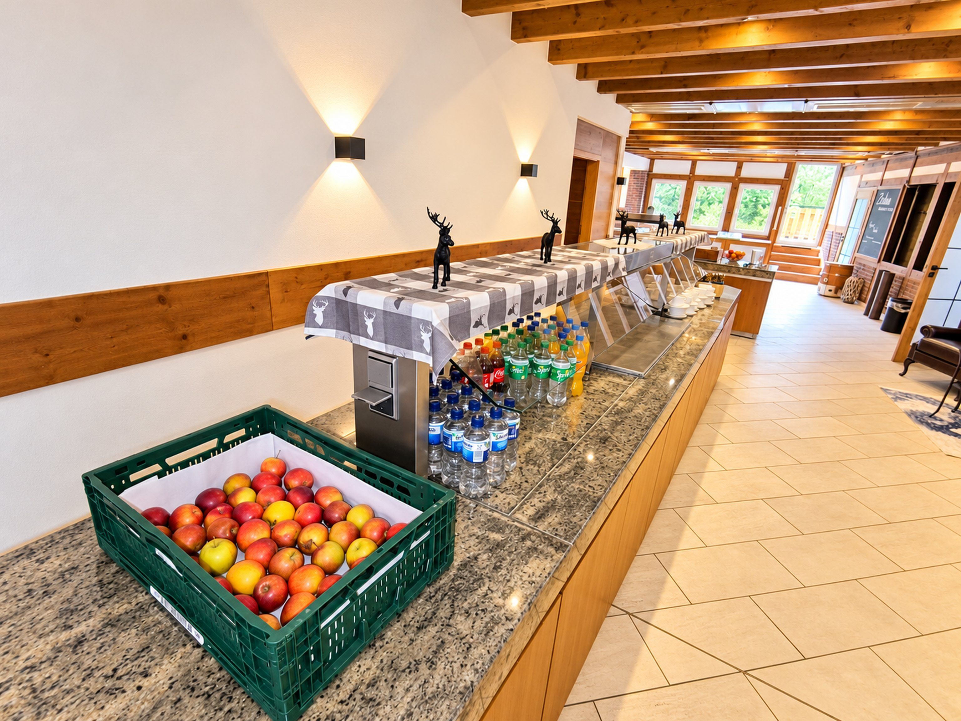 A buffet area with a fruit display, beverage dispensers, and a seating area with a view of the outdoors.