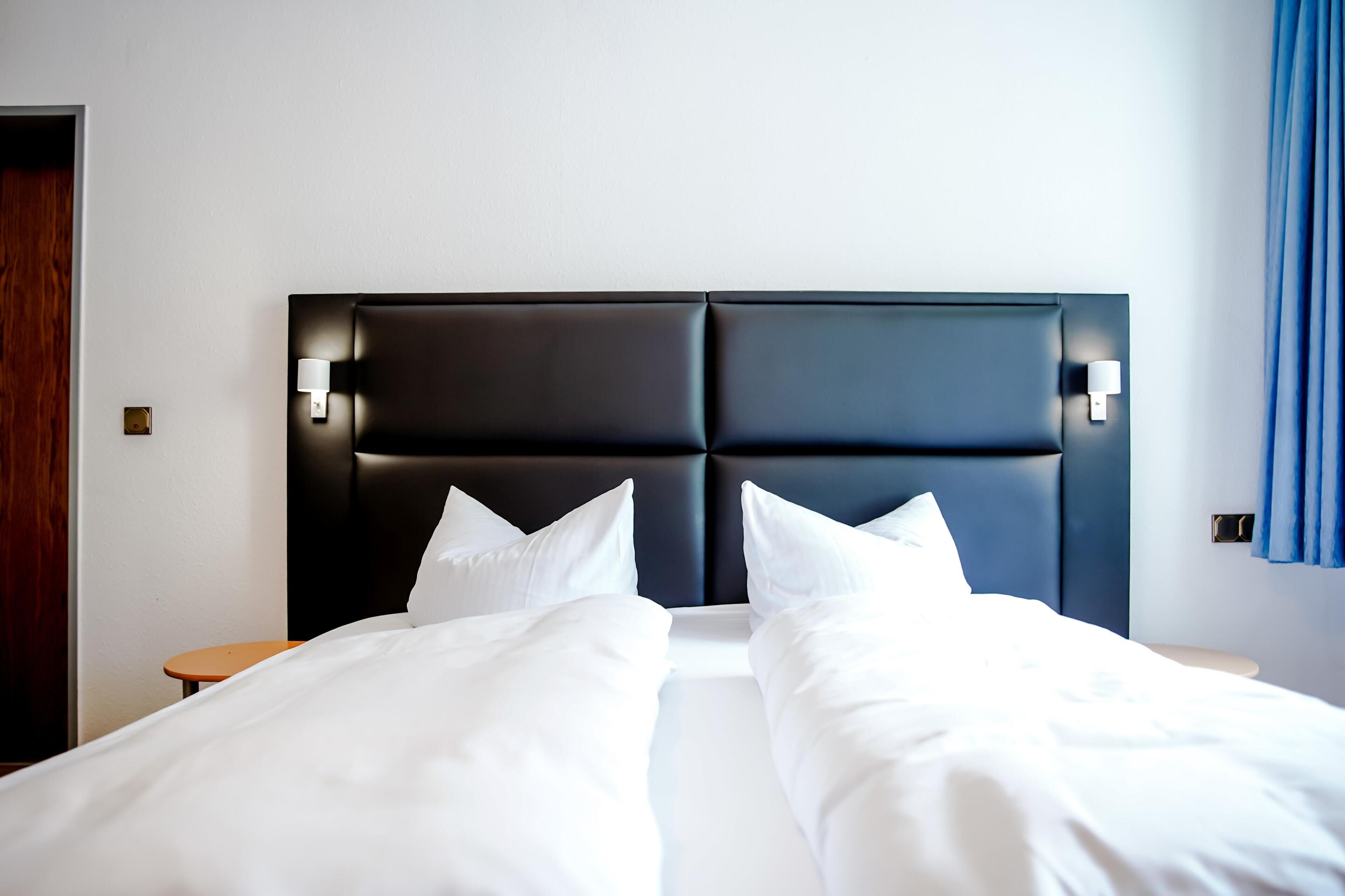 Une chambre d’hôtel avec un grand lit, deux tables de chevet et une tête de lit sombre agrémentée de lampes fixées au mur.