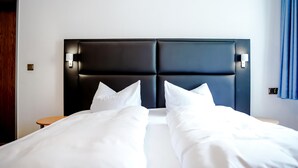 Een hotelkamer met een groot bed, twee nachtkastjes en een donker hoofdeinde met wandlampjes.