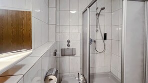 Une salle de bain moderne avec des carreaux blancs, une douche en verre, des toilettes et un sèche-mains.