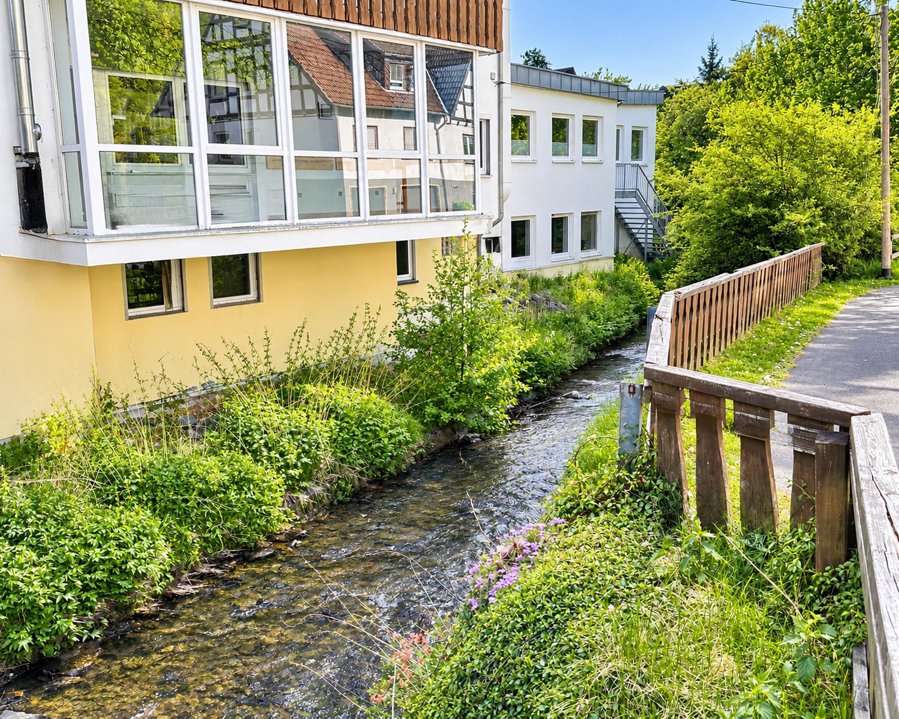 Un edificio moderno con fachada amarilla, un pequeño arroyo a su lado y un puente de madera.