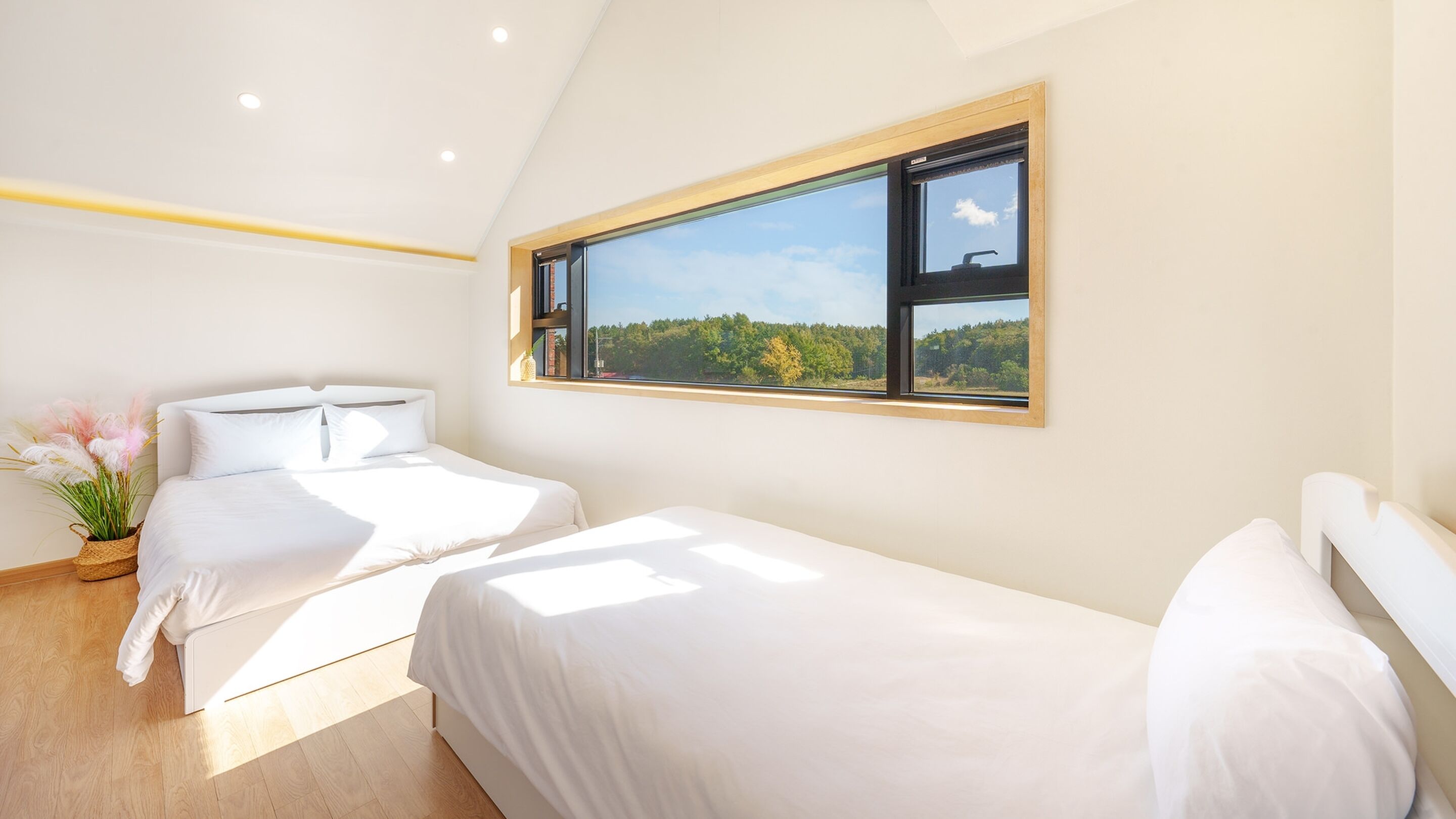 Un dormitorio moderno con dos camas, un ventanal con vistas a un bosque y una pequeña planta en el suelo.