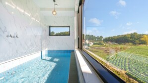 Une salle de bain moderne avec un mur en marbre, une baignoire intégrée et une grande fenêtre donnant sur un paysage verdoyant.