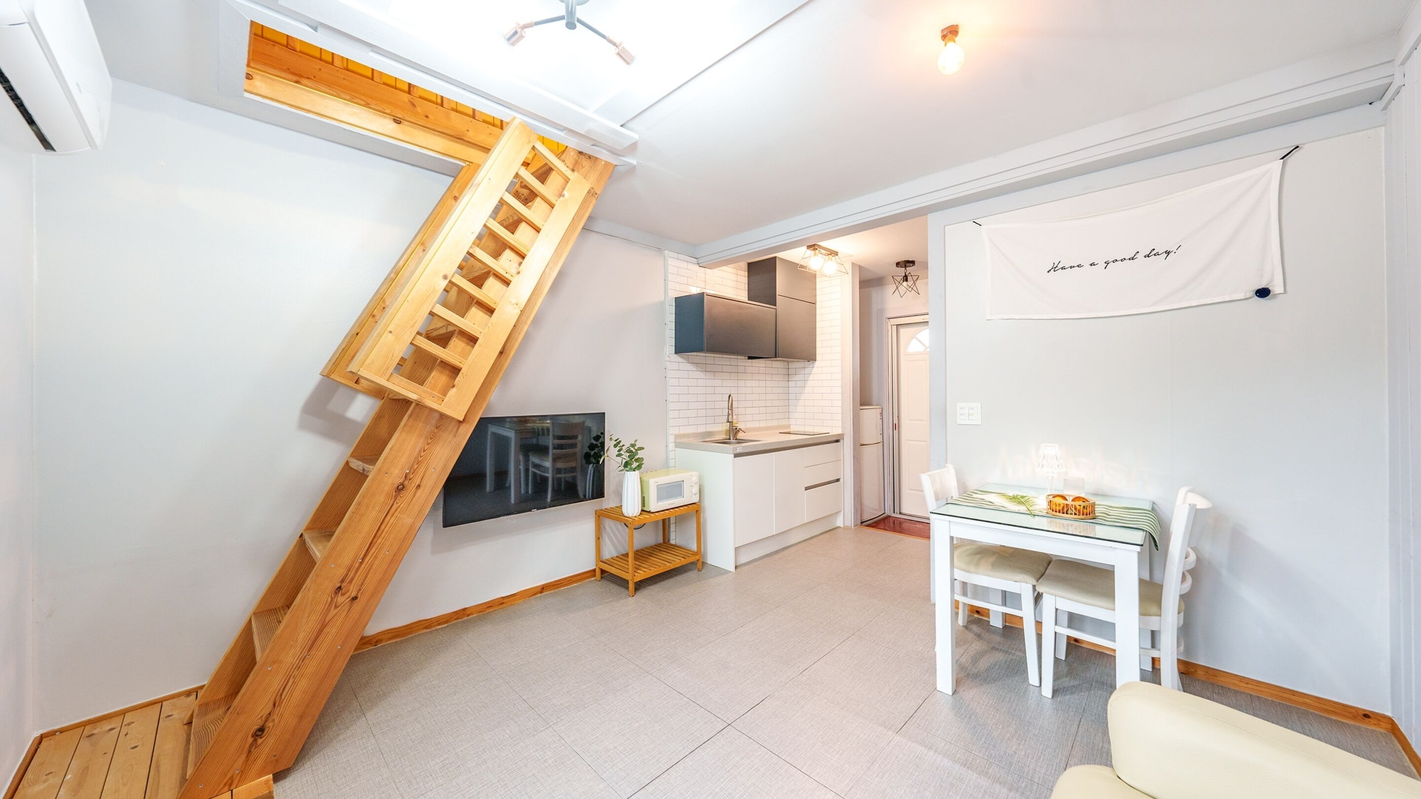 A modern kitchen with white cabinets, a wooden staircase, a dining area with a table and chairs, and a kitchen island.