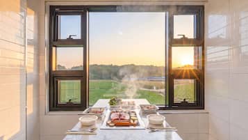 Een keuken met een groot raam, een tafel met eten, en uitzicht op een veld.