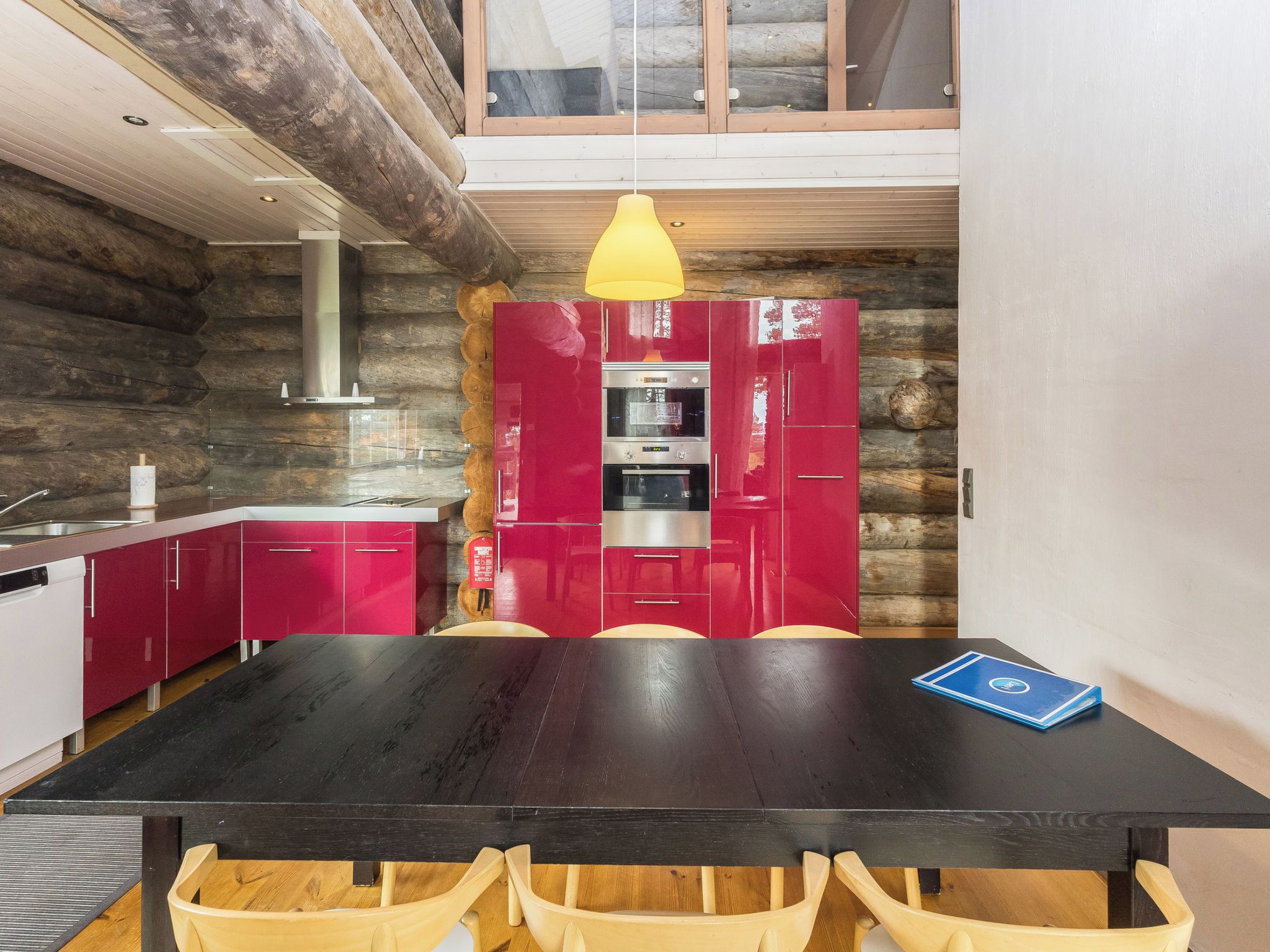 Une cuisine moderne avec des meubles de rangement rouges, une table à manger noire et un luminaire suspendu jaune.