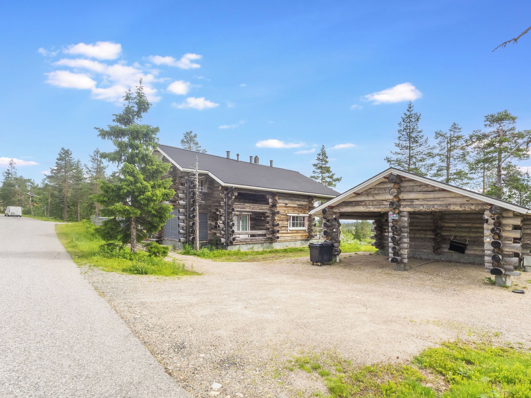Une cabane rustique en rondins de bois, avec une allée en gravier et une petite construction en bois.