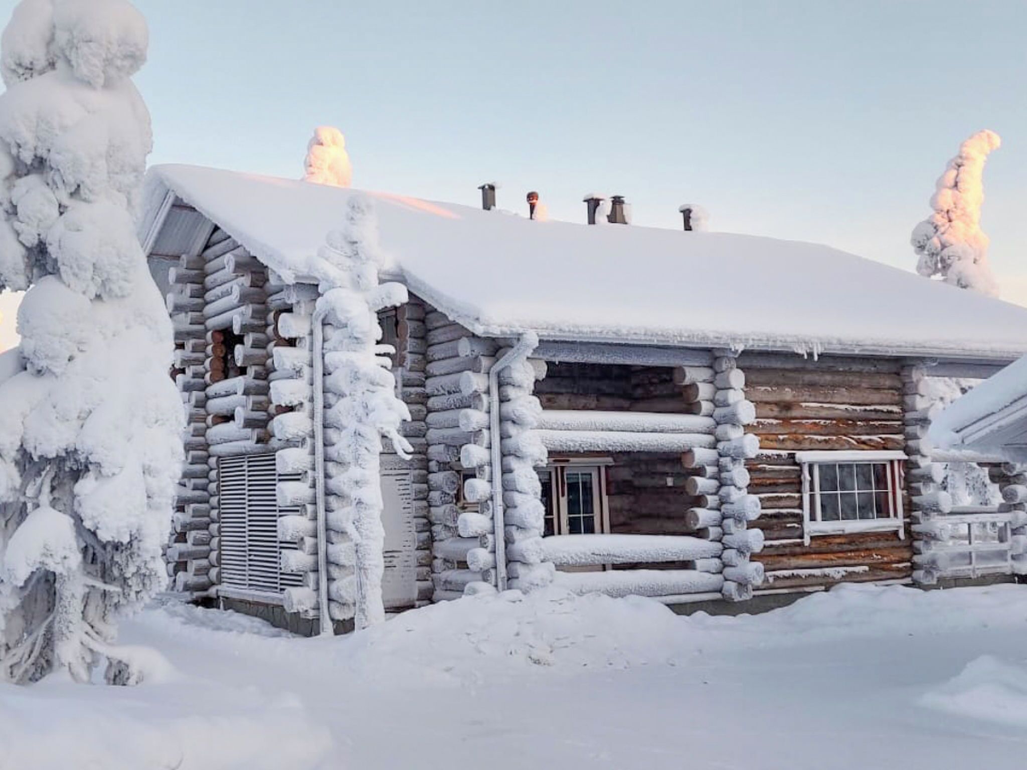 A log cabin with a snow-covered roof and chimney, surrounded by snow.