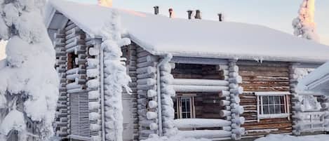Eine Blockhütte mit verschneitem Dach und Schornstein, umgeben von Schnee.